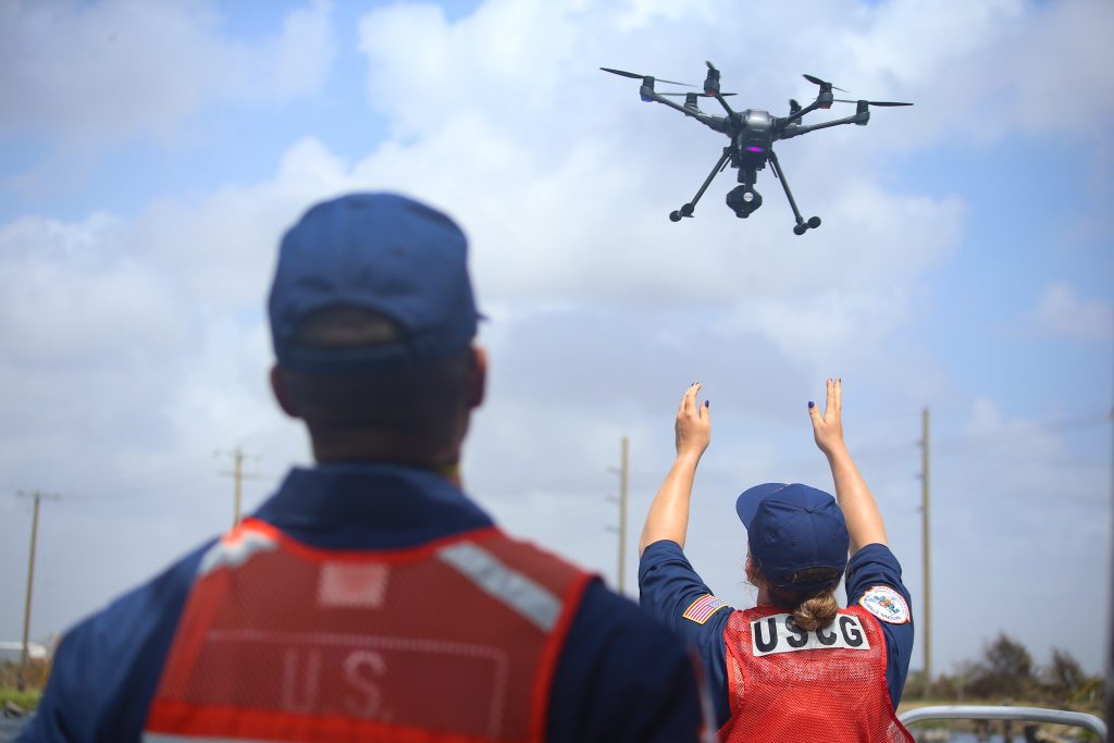 Two Coast Guard Gulf Strike Team members raise their arms as a drone lifts off in front of them.