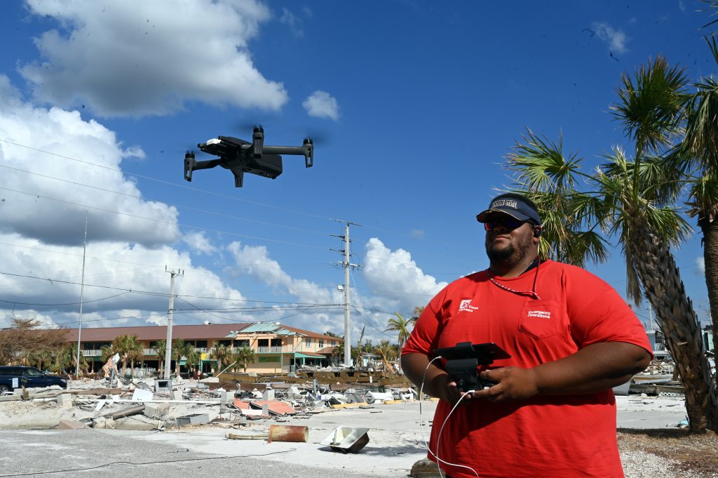 A drone pilot in a red shirt flies a quadcopter drone above storm-damaged Fort Myers Beach, Florida.